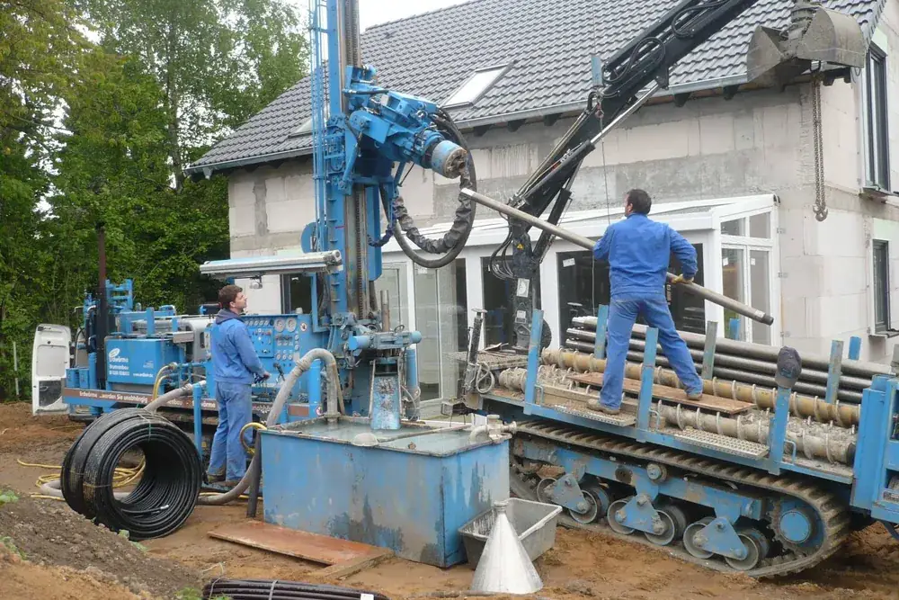 Foreuse en train de réaliser une sonde géothermique devant une maison