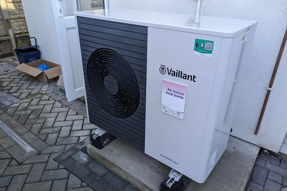 Pompe à chaleur installée devant la façade d'une maison, sur un sol pavé
